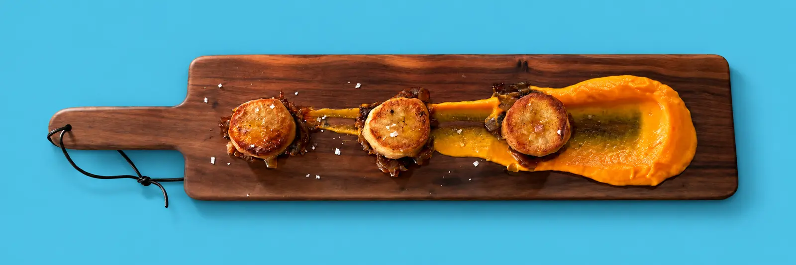 Fondant potatoes with charred onion jam and carrot mousseline on a walnut board